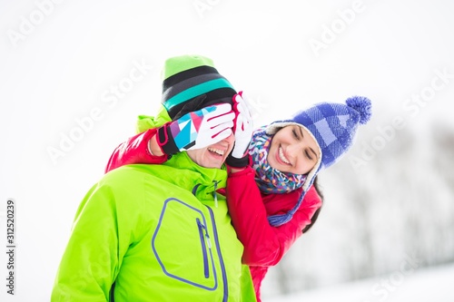 Smiling young woman covering man's eyes in winter