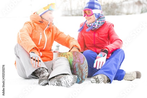 Full length of female friends with snowboard relaxing on snow