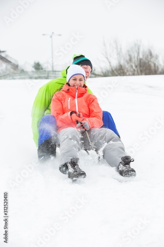 Full length of young couple sledging on snow covered land