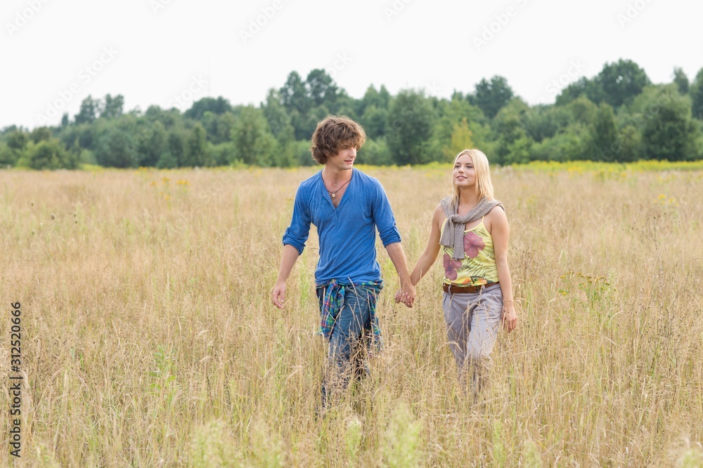 Young couple holding hands while walking through field Young couple holding hands while walking through field
