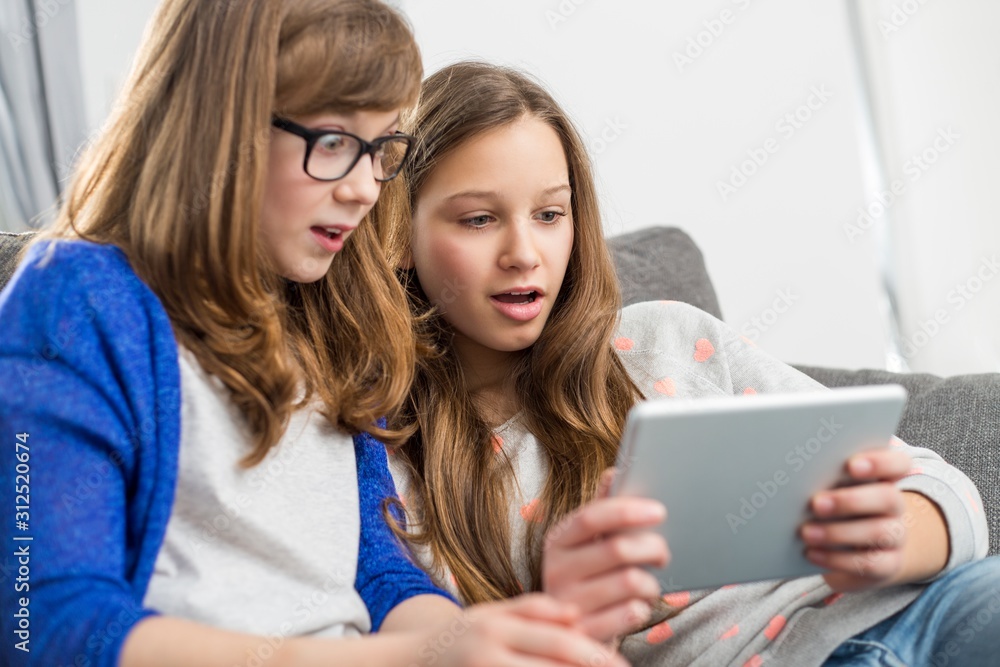 Shocked sisters using digital tablet on sofa at home Shocked sisters using digital tablet on sofa at home