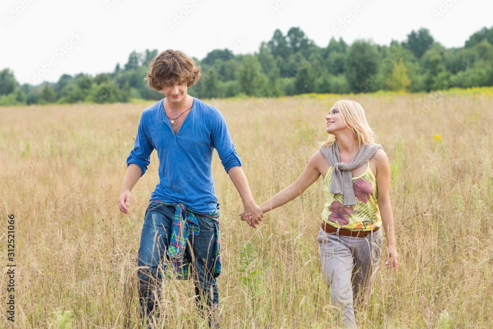Young couple holding hands while walking through field Young couple holding hands while walking through field