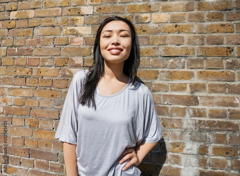 Portrait of confident young woman standing with hand on hip against brick wall