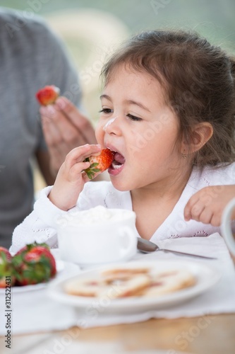 Cute little girl eating strawberry with father at breakfast table