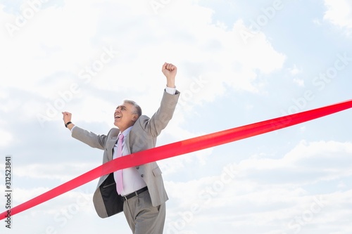 Fotografering Cheerful businessman crossing finish line against sky