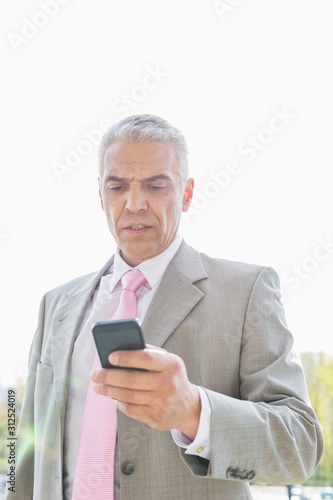 Businessman reading text message on cell phone against sky