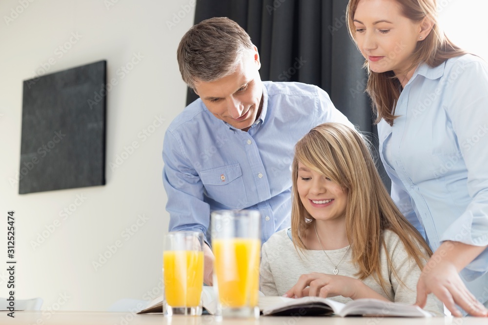 Happy parents assisting daughter in homework at home Happy parents assisting daughter in homework at home