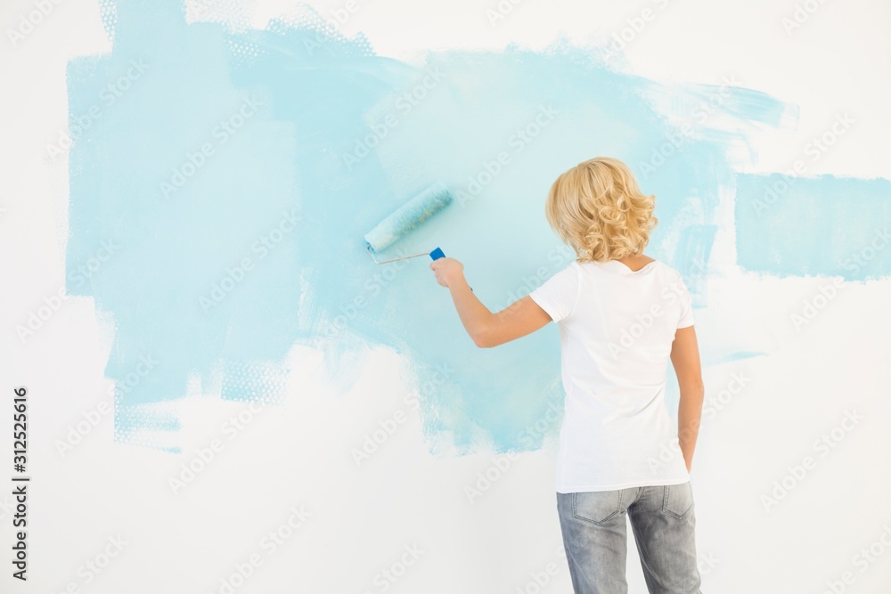 Rear view of woman painting wall with paint roller Rear view of woman painting wall with paint roller