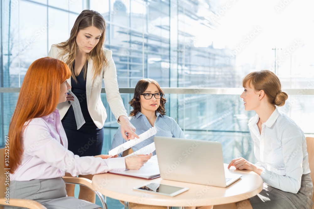 Businesswomen discussing over documents at table in office Businesswomen discussing over documents at table in office
