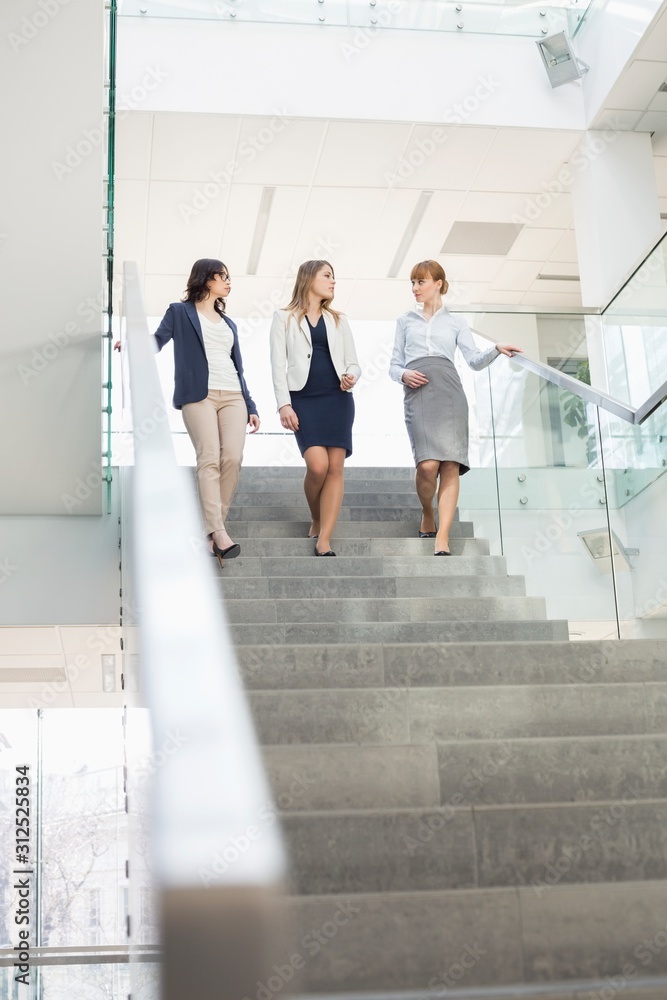 Businesswomen conversing while moving down steps in office Businesswomen conversing while moving down steps in office