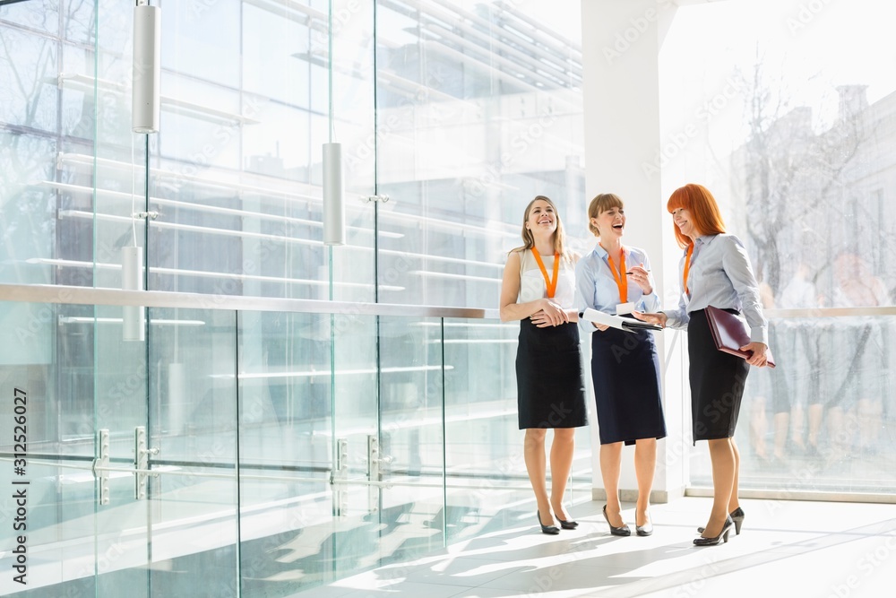 Happy businesswomen standing against glass wall in office