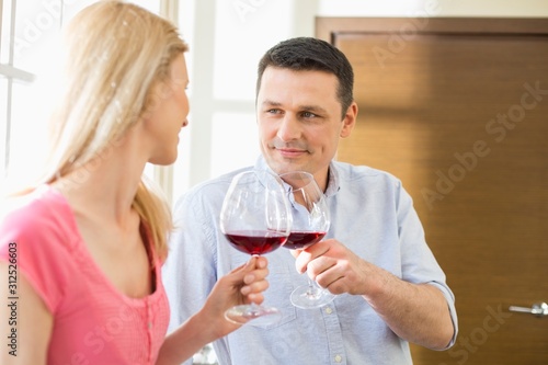 Couple toasting red wine glasses in kitchen