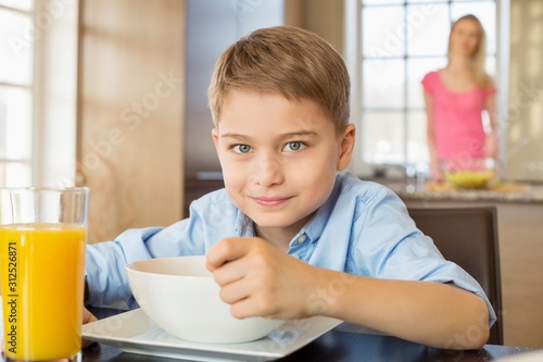Portrait of boy having breakfast at table with mother standing in background