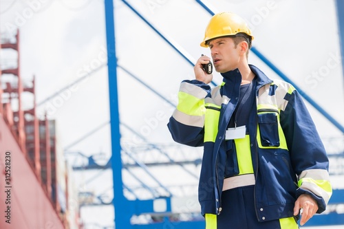 Mid adult male worker using walkie-talkie in shipping yard