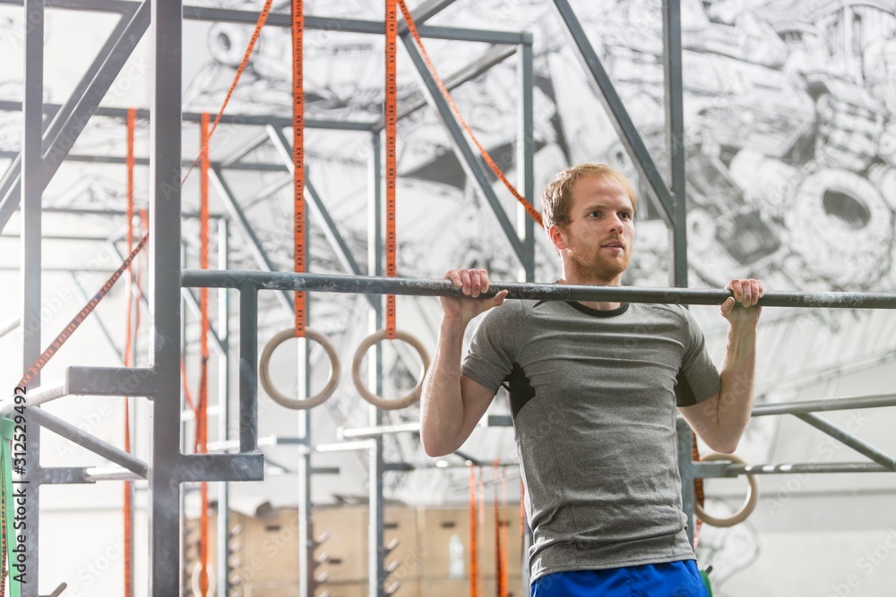 Confident man doing chin-ups in crossfit gym