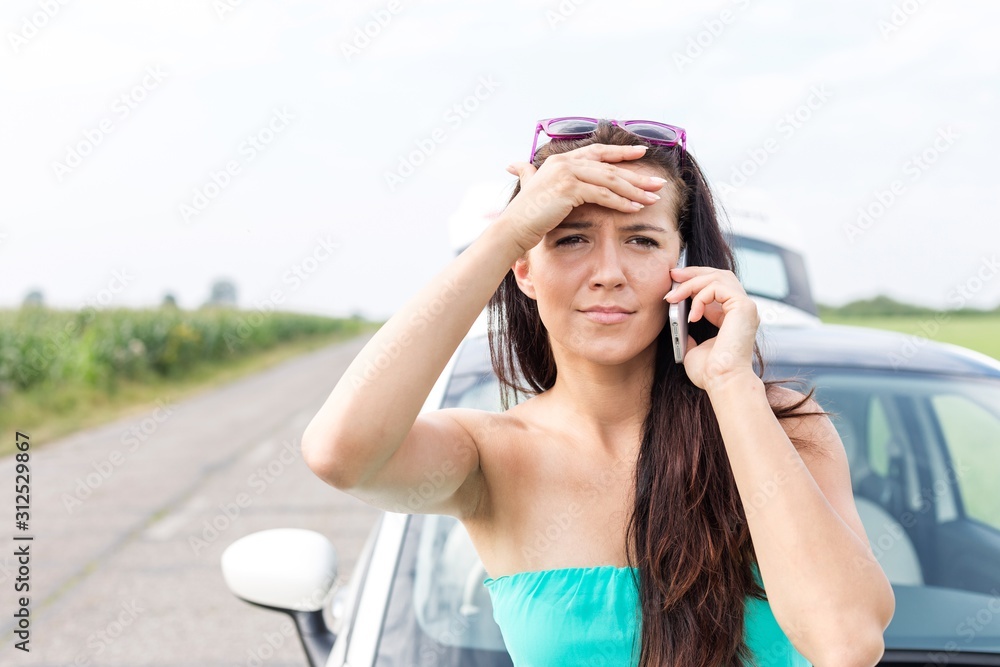 Portrait of tensed woman using cell phone against broken down car on road