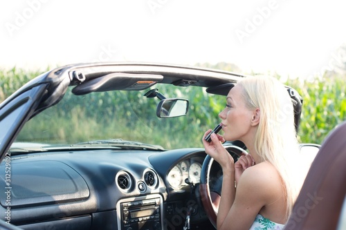 Rear view of woman applying lipstick in convertible © moodboard
