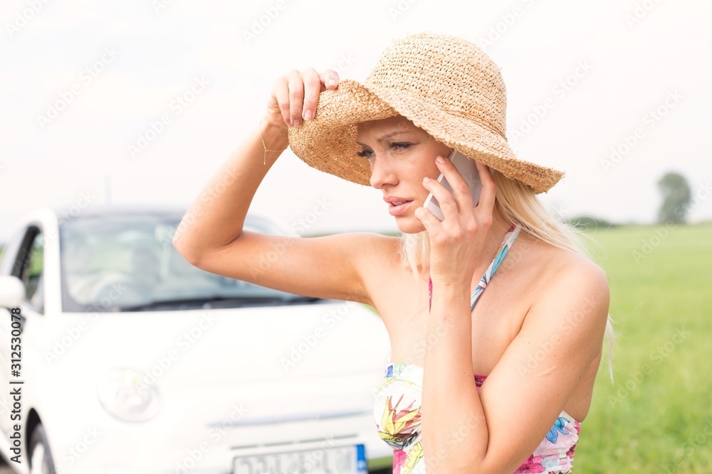 Frustrated woman using cell phone by broken down car