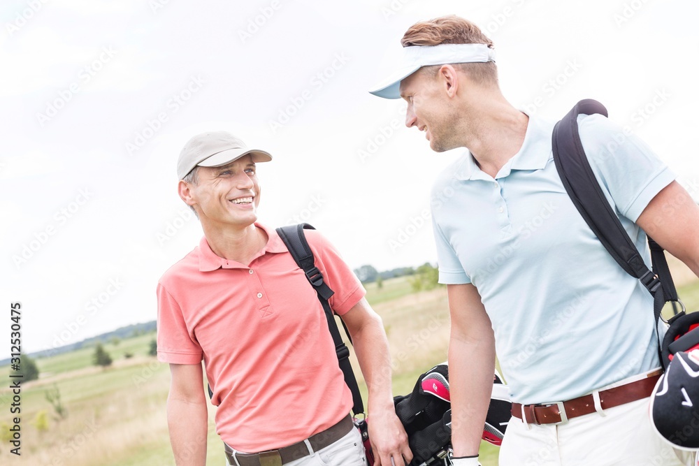 Happy male golfers conversing against clear sky Happy male golfers conversing against clear sky