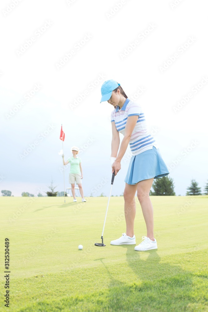 Woman playing golf with female friend holding flag against sky Woman playing golf with female friend holding flag against sky