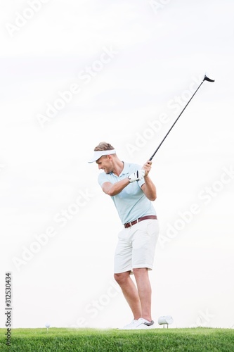 Full-length of mid-adult man swinging golf club against clear sky