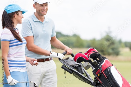 Happy friends with bag talking at golf course