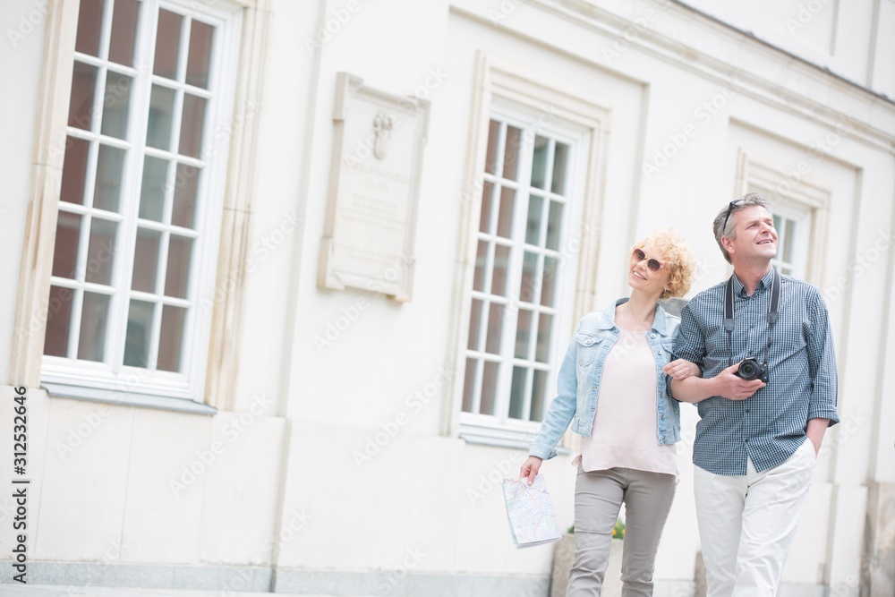 Happy middle-aged tourist couple walking arm in arm by building Happy middle-aged tourist couple walking arm in arm by building