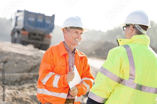 Happy engineer discussing with colleague at construction site on sunny day