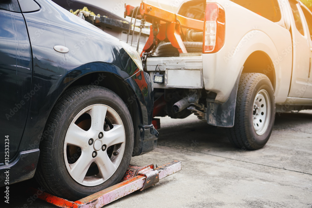 Tow truck picking up and towing old broken down car on a roadside ...