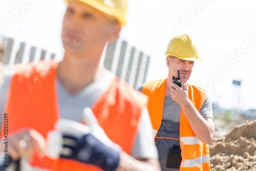 Middle-aged male worker using walkie-talkie with colleague in foreground at construction site
