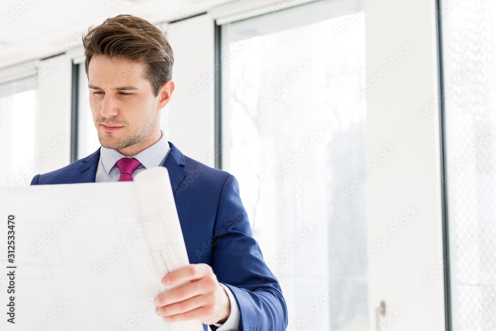 Confident young businessman reading blueprint in new office Confident young businessman reading blueprint in new office