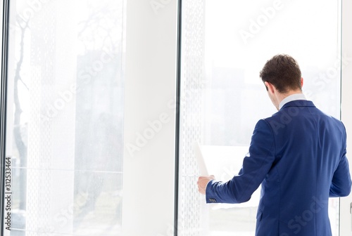 Rear view of young businessman reading blueprint in new office