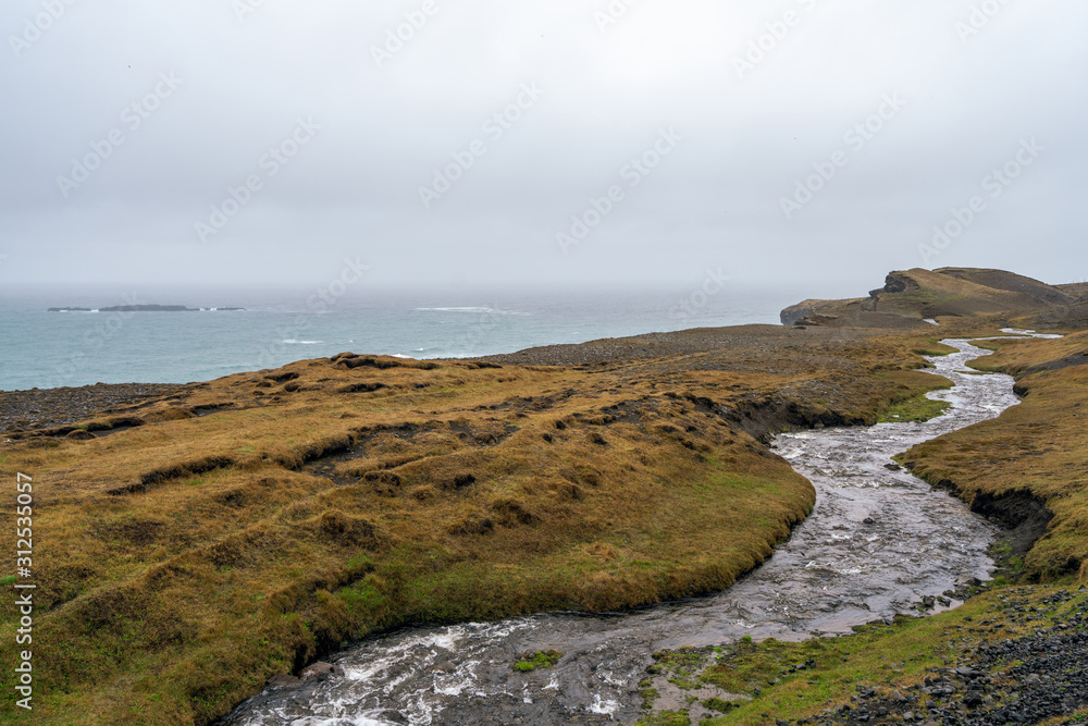 Ketubjorg bird cliffs with creek infront as leading lines towards the ocean during rainy weather. Icelandic landscape scenery concept. Ketubjorg bird cliffs with creek infront as leading lines towards the ocean during rainy weather. Icelandic landscape scenery concept.