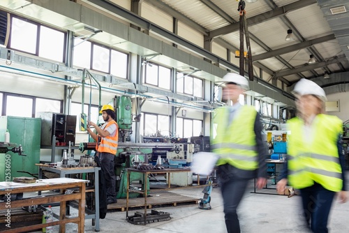 Blurred motion of business people with manual worker in background at industry