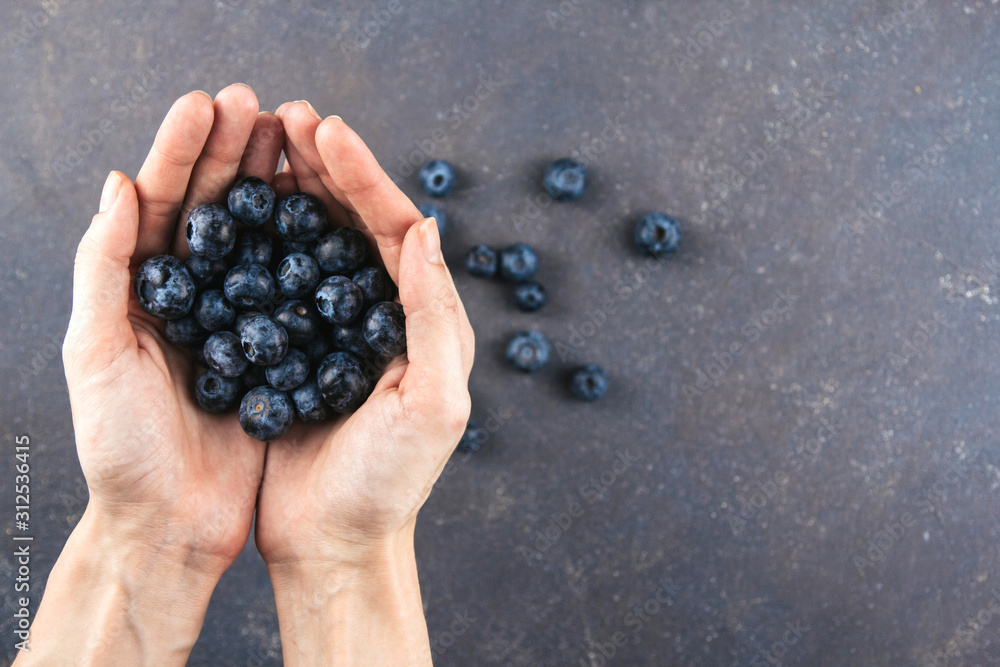 Large ripe blueberries in female hands on a gray background. A handful of blueberries. Large ripe blueberries in female hands on a gray background. A handful of blueberries.