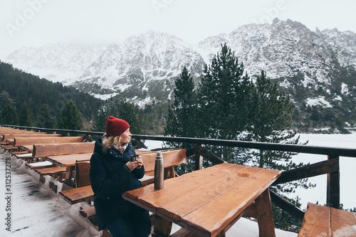 Woman having a hot drink from thermo cup overlooking snowcapped High Tatra mountains peaks