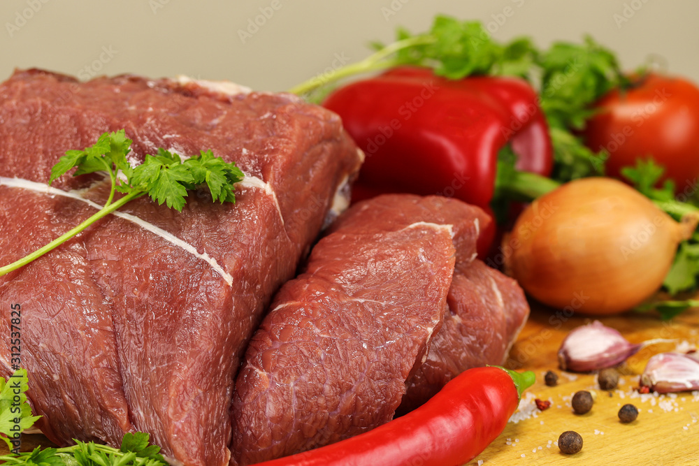 Fresh raw pork pulp and vegetables lie on a wooden cutting board on a gray background