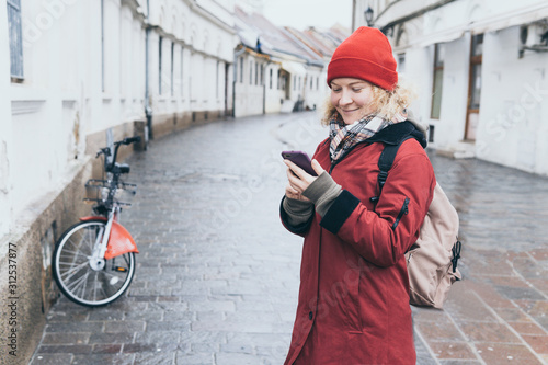 Woman in red coat looking at her mobile phone screen on the street of European town