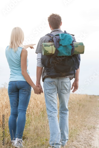 Rear view of female hiker showing something to man on field