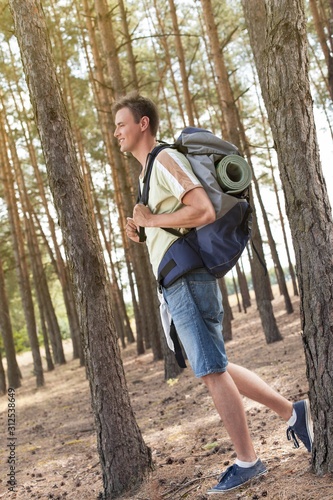 Full length side view of male hiker with backpack walking in forest
