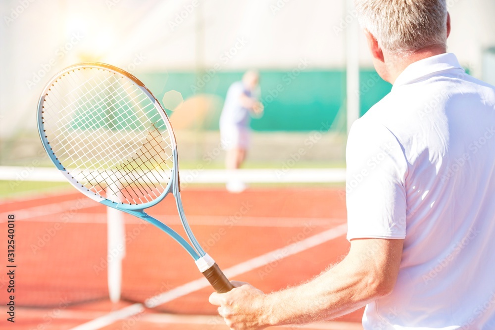 Rear view of mature man holding racket while playing with friend on tennis court