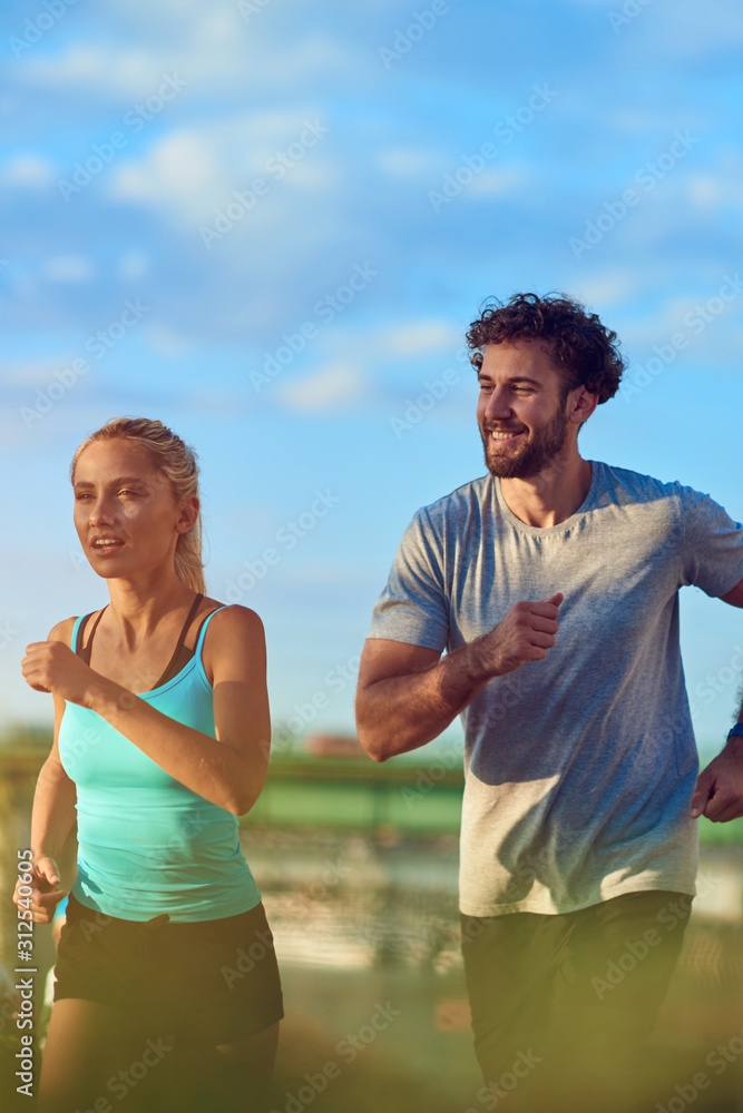 Modern woman and man jogging / exercising in urban surroundings near the river.