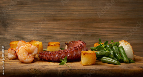 Grilled octopus tentacle on a wooden cut board served with shrimps photo