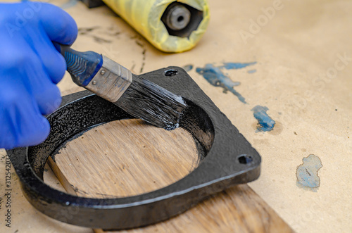 Hand in blue rubber gloves paints metal parts with black paint brush.