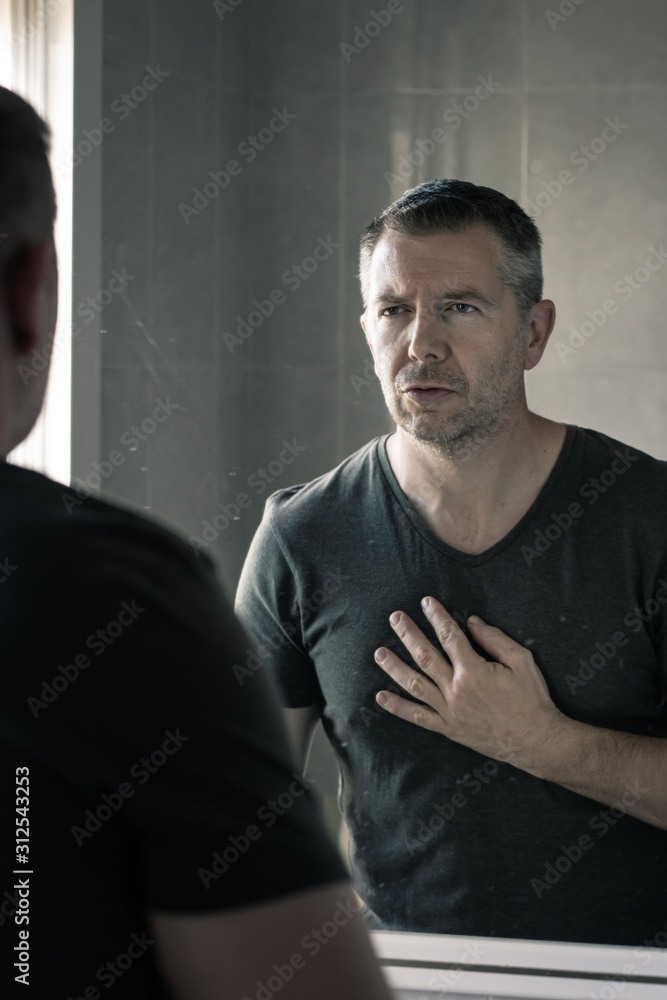 Man in grey v-neck tshirt staring at himself in bathroom mirror