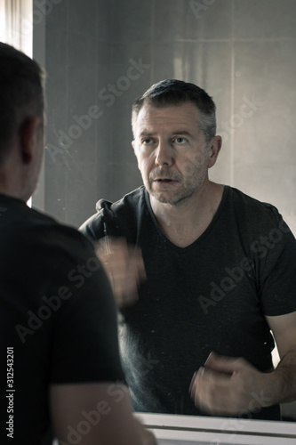 Man in grey v-neck tshirt staring at himself in bathroom mirror