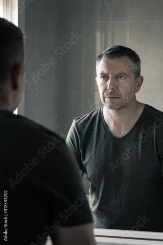 Man in grey v-neck tshirt staring at himself in bathroom mirror