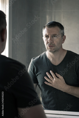 Man in grey v-neck tshirt staring at himself in bathroom mirror