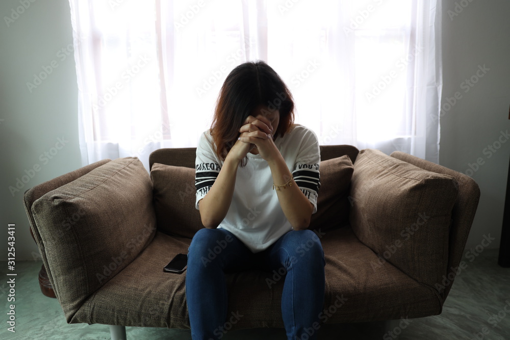 Asian woman stressful face with her hands cover of face. Short hair asian Woman feel lonely and sad sit alone on sofa bed in the living room Asian woman stressful face with her hands cover of face. Short hair asian Woman feel lonely and sad sit alone on sofa bed in the living room