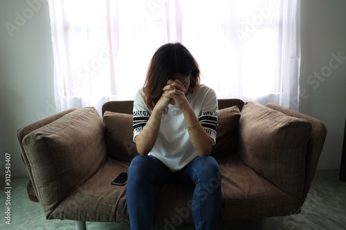 Asian woman stressful face with her hands cover of face. Short hair asian Woman feel lonely and sad sit alone on sofa bed in the living room